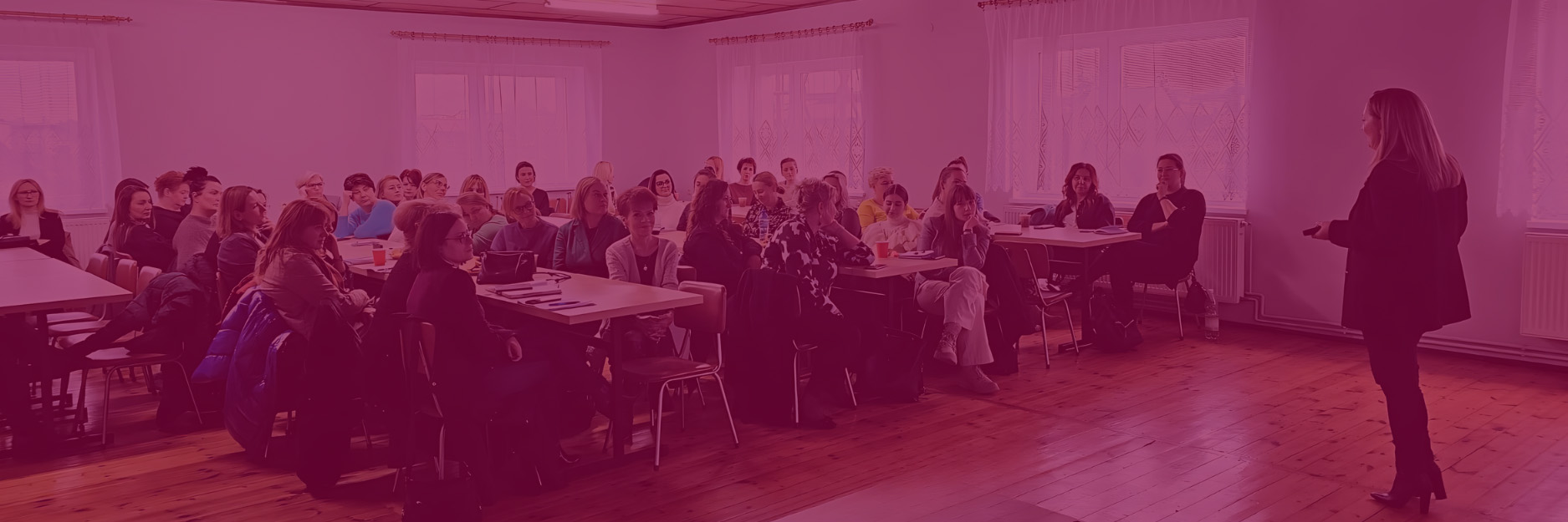 Zdjęcie prezentuje osobę mówiącą do dużej grupy osób, które siedzą.